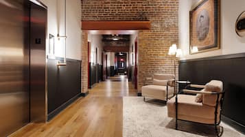 A hotel corridor with a wooden floor, a seating area with a patterned rug, and a framed portrait on the wall.
