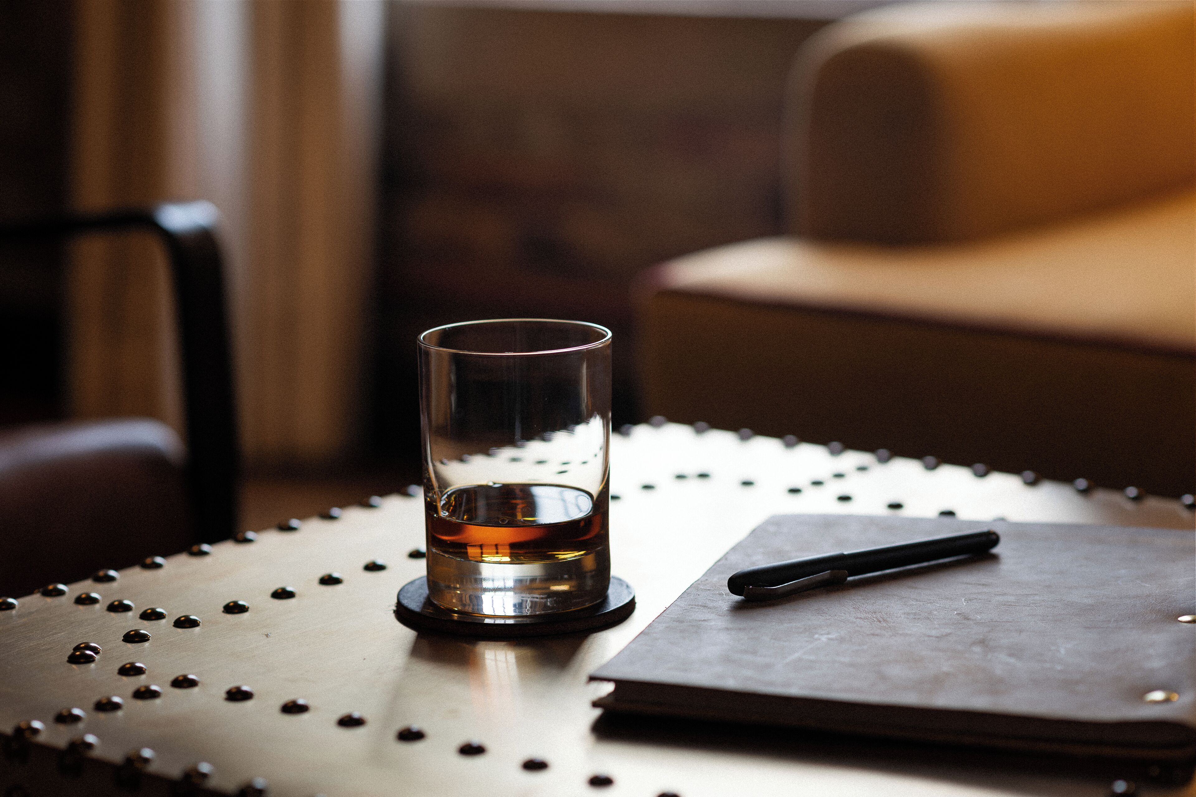 A glass of whiskey on a round table with a pen and a notebook.
