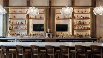 A bar area with multiple shelves of liquor bottles, bar stools, and hanging light fixtures.