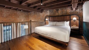 A bedroom with a wooden bed, brick walls, and a balcony with a railing. - The Delegate (Frankfort)