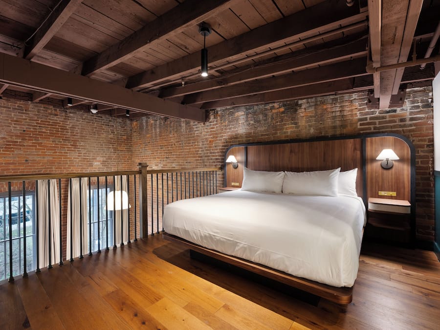 A bedroom with a wooden bed, brick walls, and a balcony with a railing.