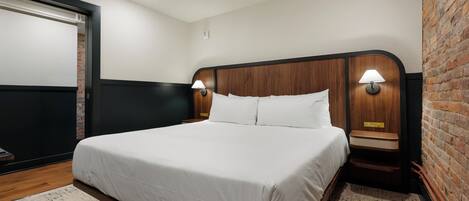 A neatly made bed in a hotel room with a wooden headboard, two bedside lamps, and a brick accent wall.