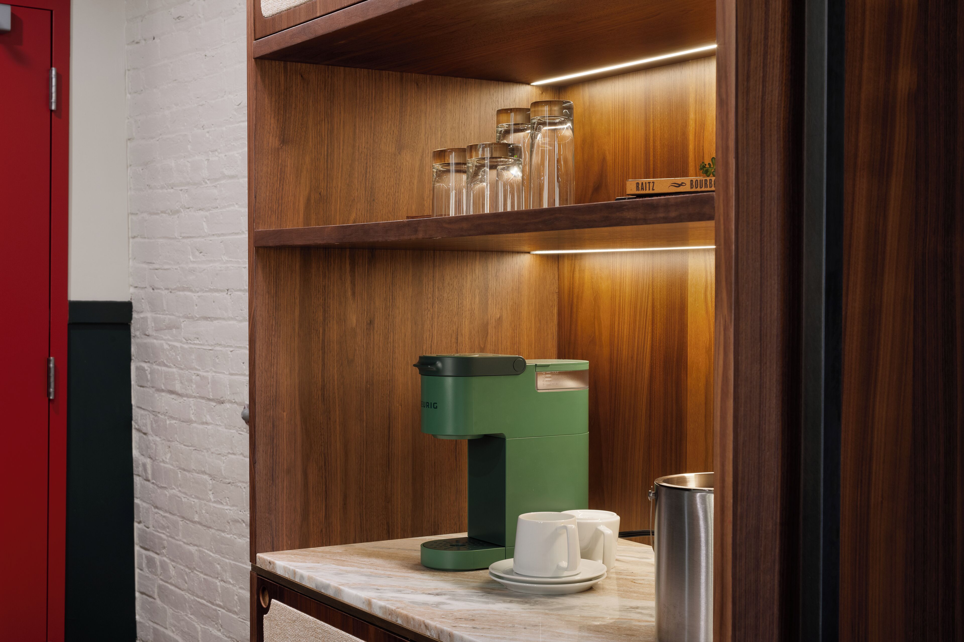 A modern kitchen with a coffee machine, a marble countertop, and a shelf with glassware.