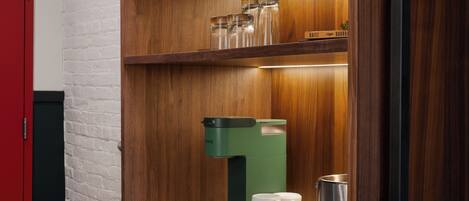 A modern kitchen with a coffee machine, a marble countertop, and a shelf with glassware.