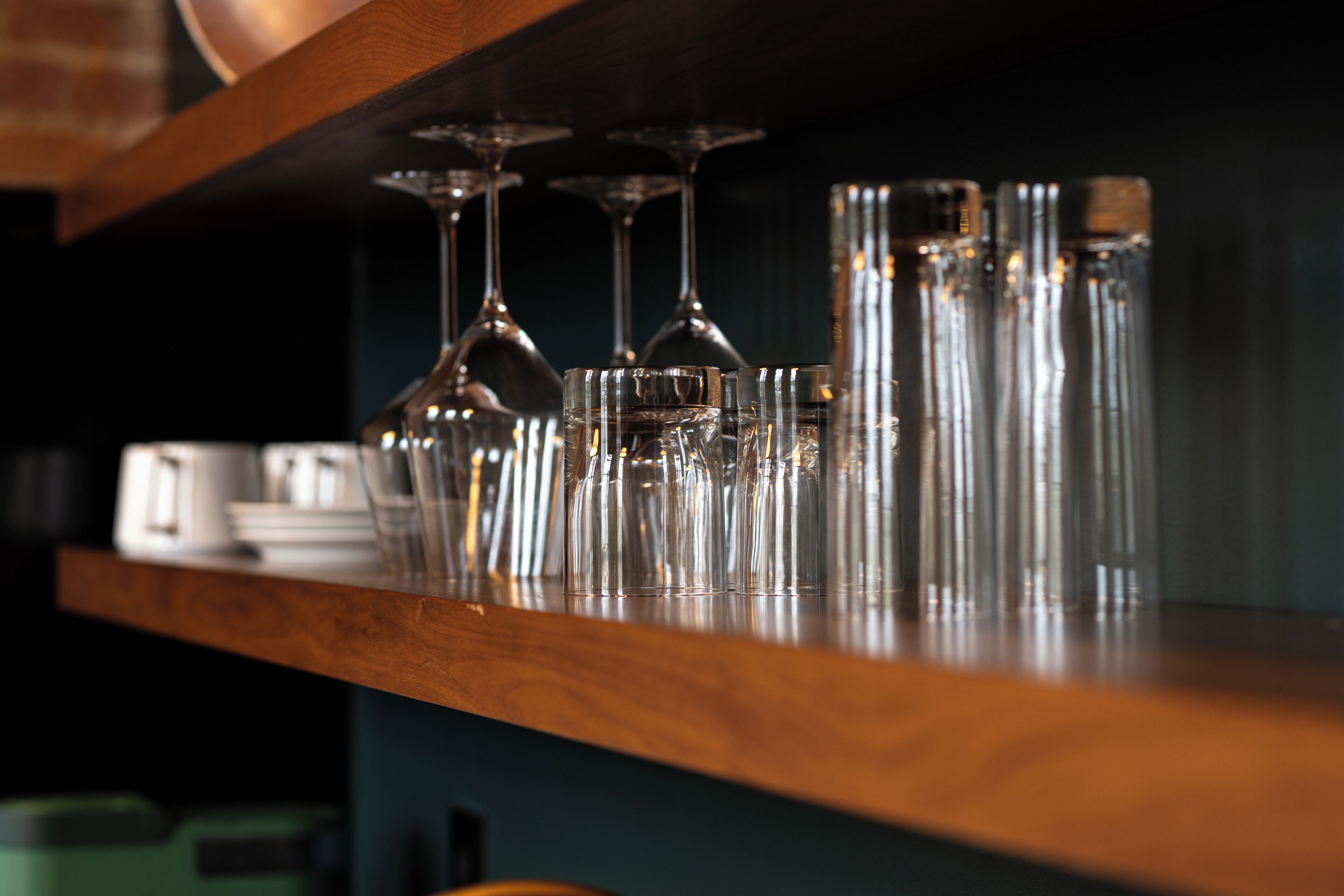 A wooden shelf with multiple wine glasses and bottles.
