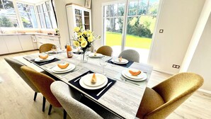 A dining area with a long table set for six, surrounded by chairs. There is a window with a view of greenery outside.