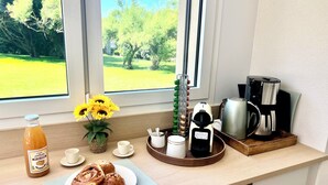 A breakfast setup with a bottle, flowers, pastries, and coffee-making equipment on a kitchen counter.