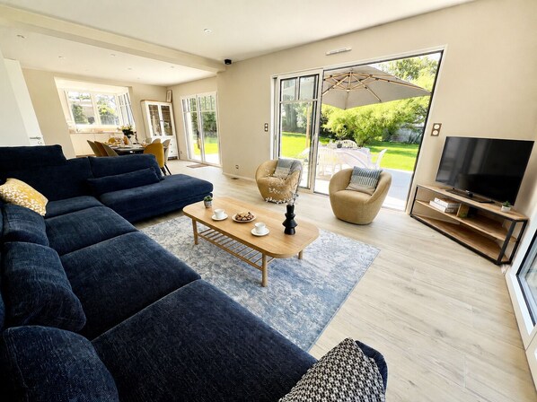 A modern living room with a sectional sofa, a coffee table, a TV stand, and a sliding glass door leading to a garden.