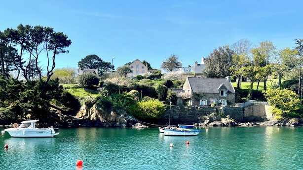 A coastal town with boats on the water, stone buildings, and greenery.