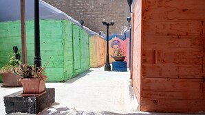 Un espacio al aire libre cubierto con estructuras de madera de colores, suelo de concreto y techo de paja.