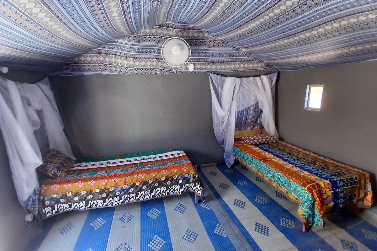 A room with two beds, patterned rugs, a ceiling fan, and a small window.