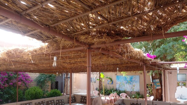 Un área de estar al aire libre con techo de paja, bancos acolchados y suelo de mosaicos.