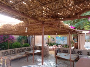 An outdoor seating area with thatched roof, cushioned benches, and a mosaic-tiled floor. - Par 4 Chemins - Atypical stopover (Nouakchott)