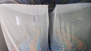 Dos ventanas con cortinas estampadas, piso de baldosas y un banco azul.