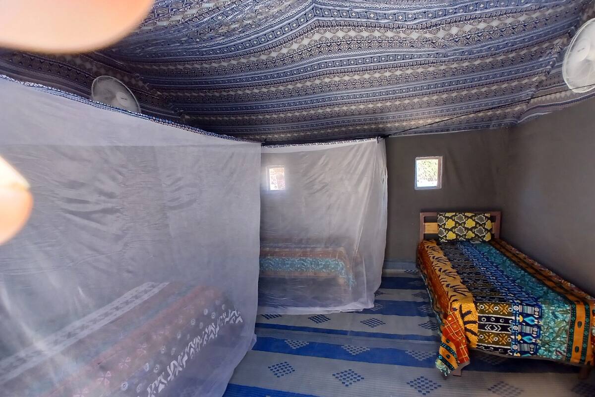 A room with a patterned floor, a bed with a colorful bedspread, a mosquito net, and a small window.