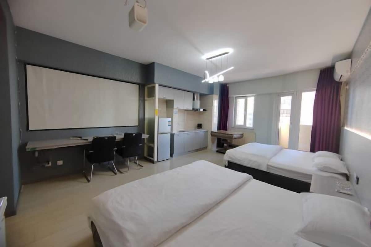 A hotel room with two beds, a desk, a chair, a TV, and a kitchenette.