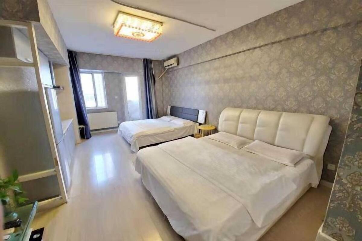 A hotel room with two beds, a small bedside table, a ceiling light, and a window with curtains.