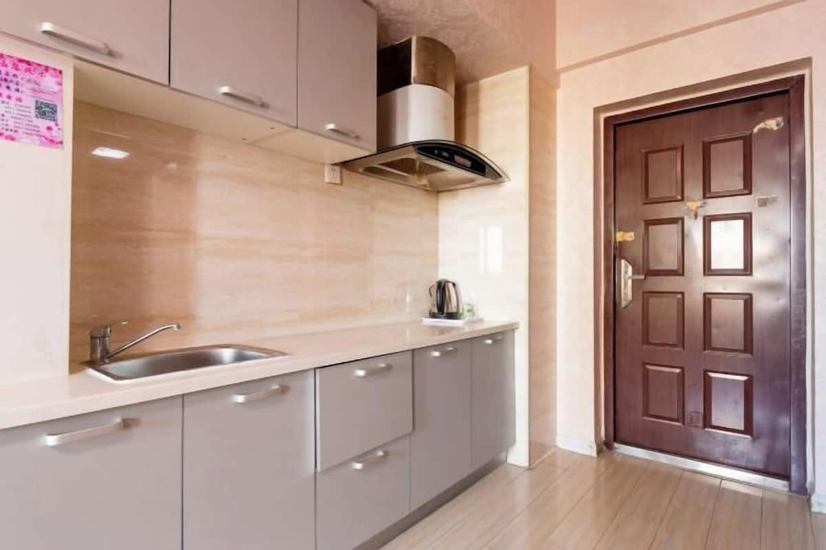 A kitchen with a stainless steel sink, grey cabinets, a stainless hood, and a brown door.