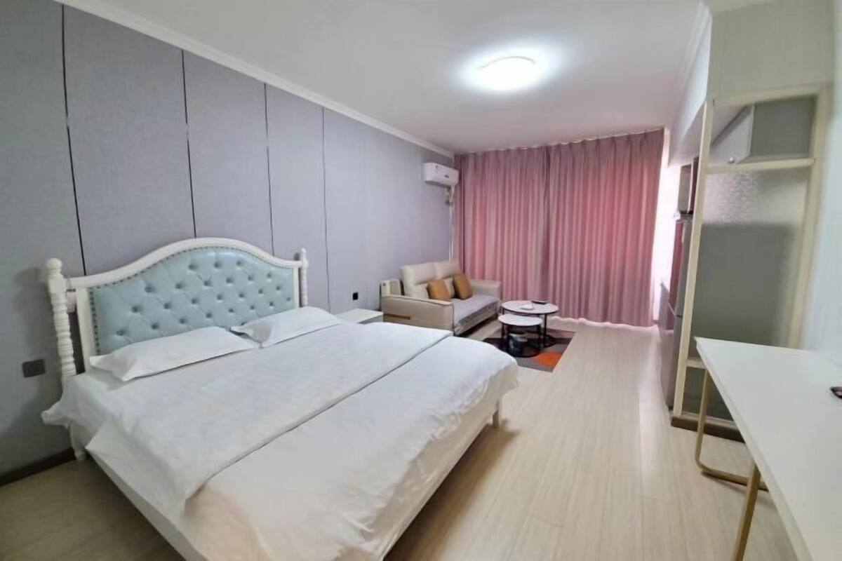A hotel room with a bed, a sofa, a small table, and an air conditioning unit.