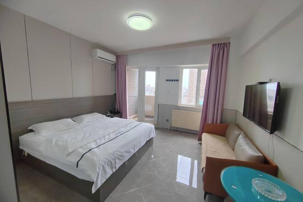 A hotel room with a bed, a sofa, a TV, and a window with curtains.