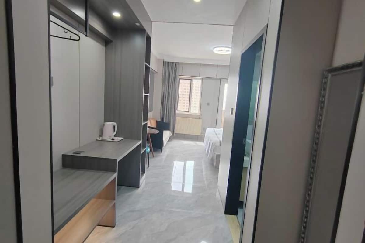 A modern hotel room with a bed, a desk, a chair, and a window.