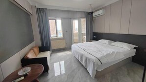 A modern hotel room with a bed, a sofa, a small table, and a window with curtains.