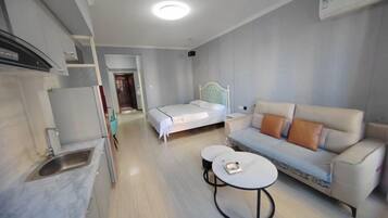 Una habitación de hotel compacta con kitchenette, una cama, un sofá y una pequeña mesa redonda.