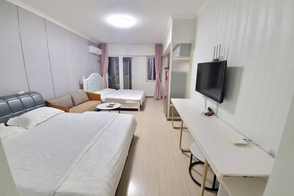 A hotel room with a bed, a sofa, a desk, a TV, and a window with curtains.