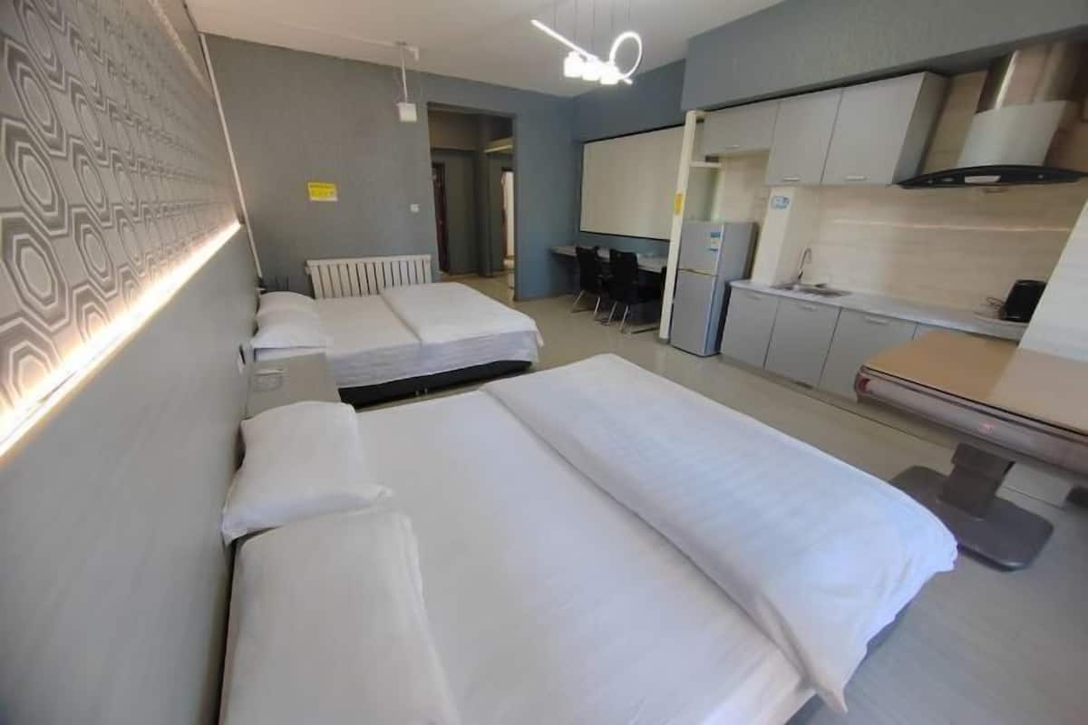 A hotel room with two beds, a kitchenette, a desk, and a seating area.
