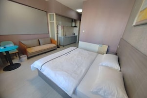 Una habitación de hotel con cama, una mesita, un sofá y una kitchenette al fondo.