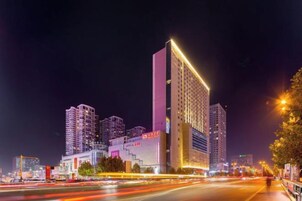 Een hoog gebouw met meerdere verdiepingen, verlicht door kunstlicht, omgeven door andere hoge gebouwen.