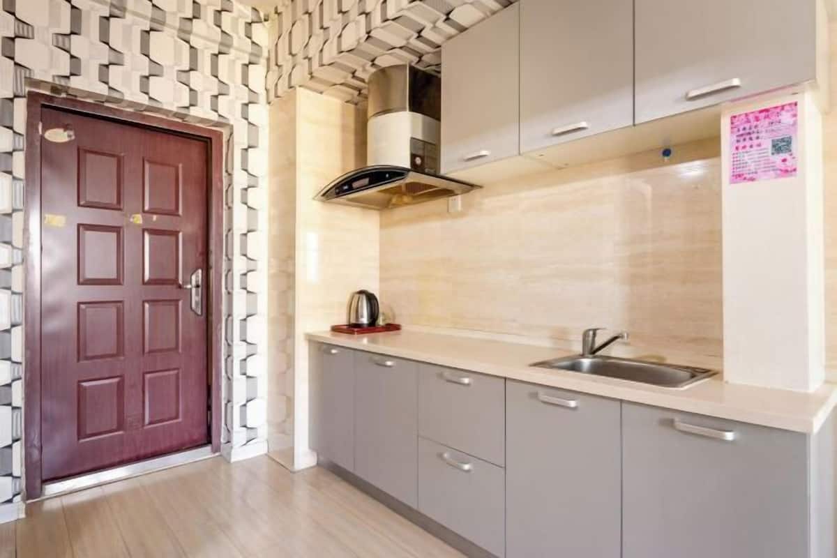 A kitchen with a patterned wall, a red door, grey cabinets, and a stainless steel sink.