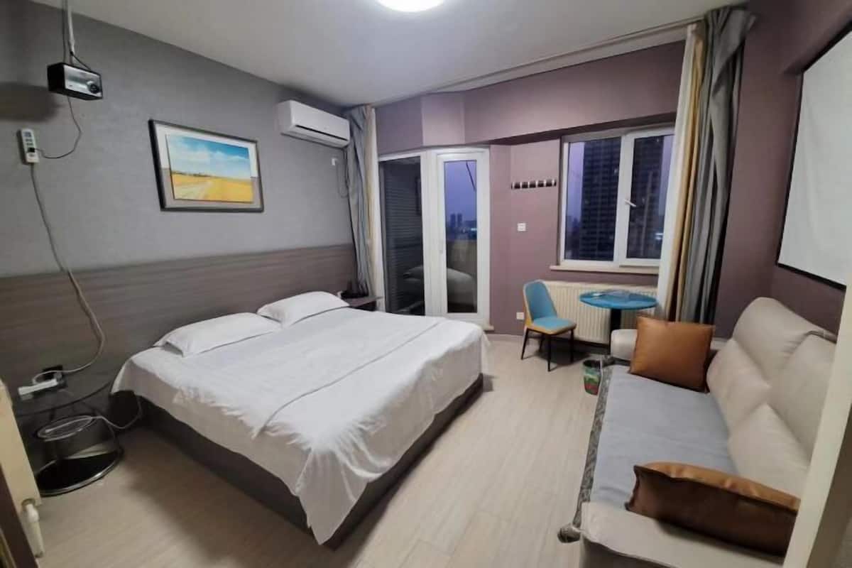 A hotel room with a bed, a sofa, a small table, and a window with curtains.