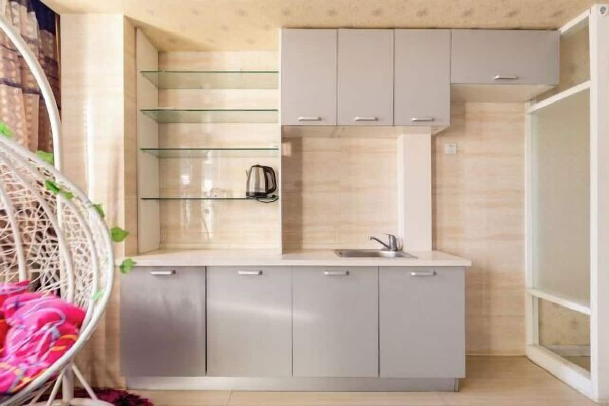 A compact kitchen with a sink, cabinets, and a glass shelf unit.
