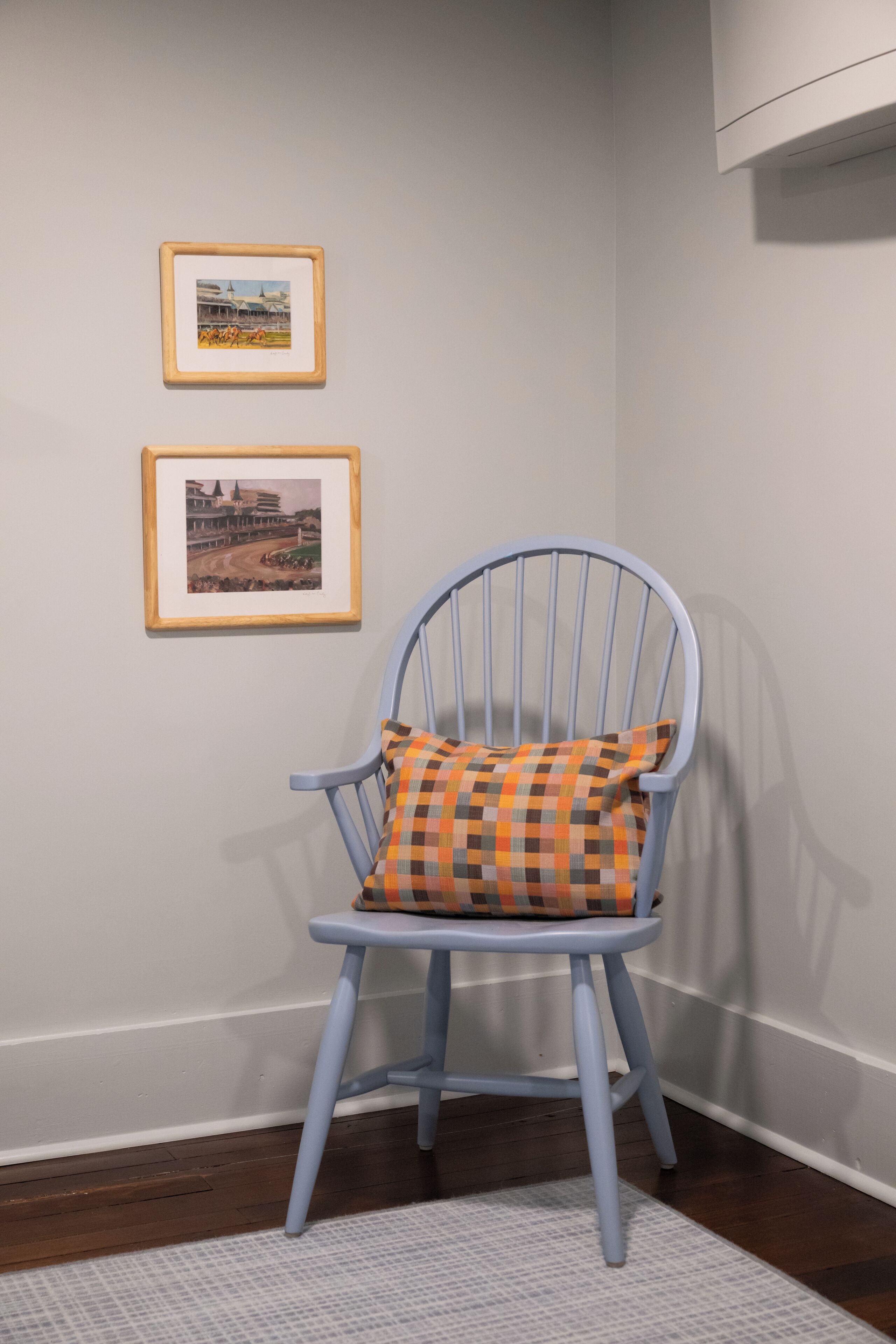 Une pièce avec une chaise bleue dotée d’un coussin à carreaux, un tableau encadré accroché au mur et un tapis à motifs sur le sol.