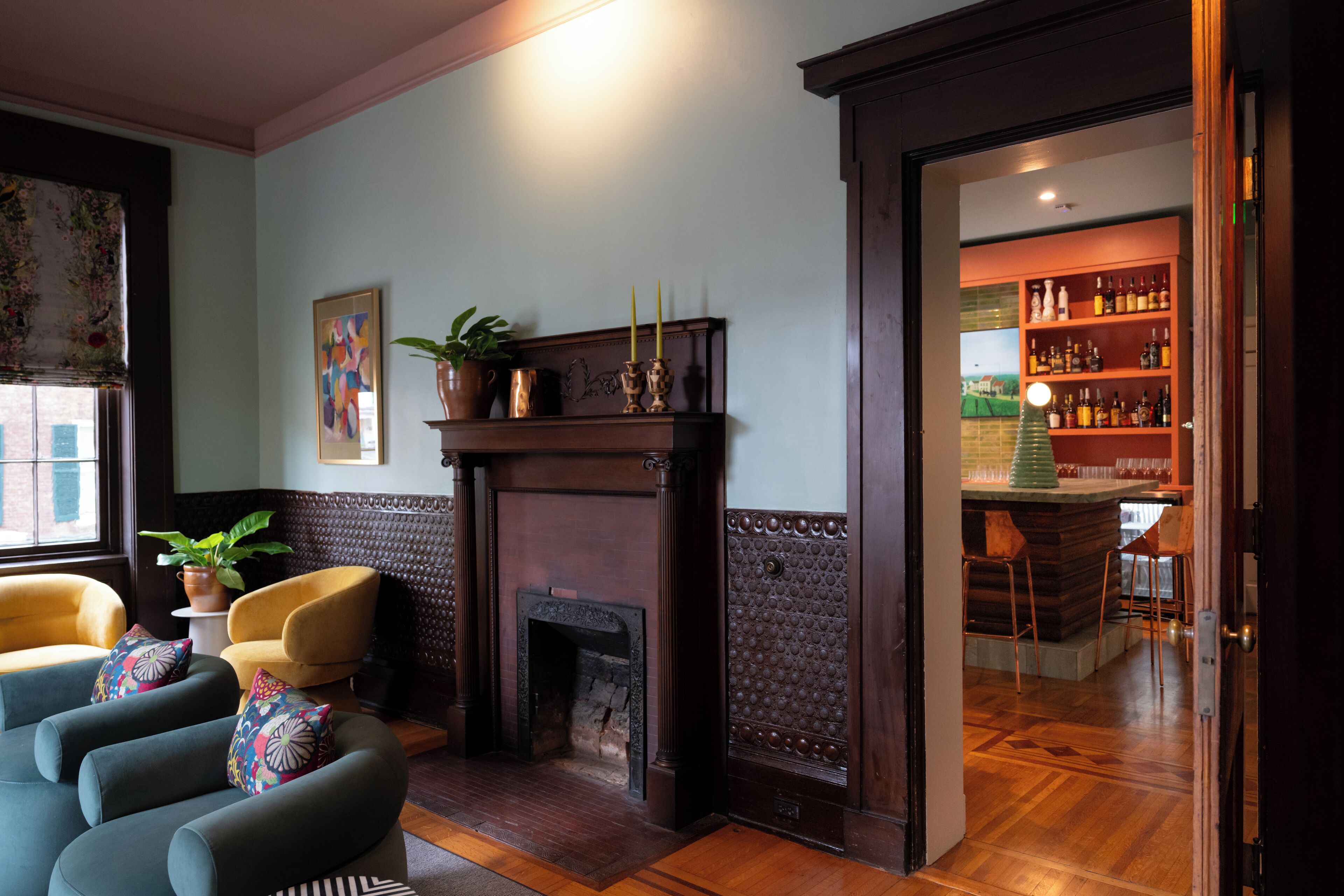Un salon chaleureux avec une cheminée, des sièges confortables et un coin bar visible à travers une porte ouverte.