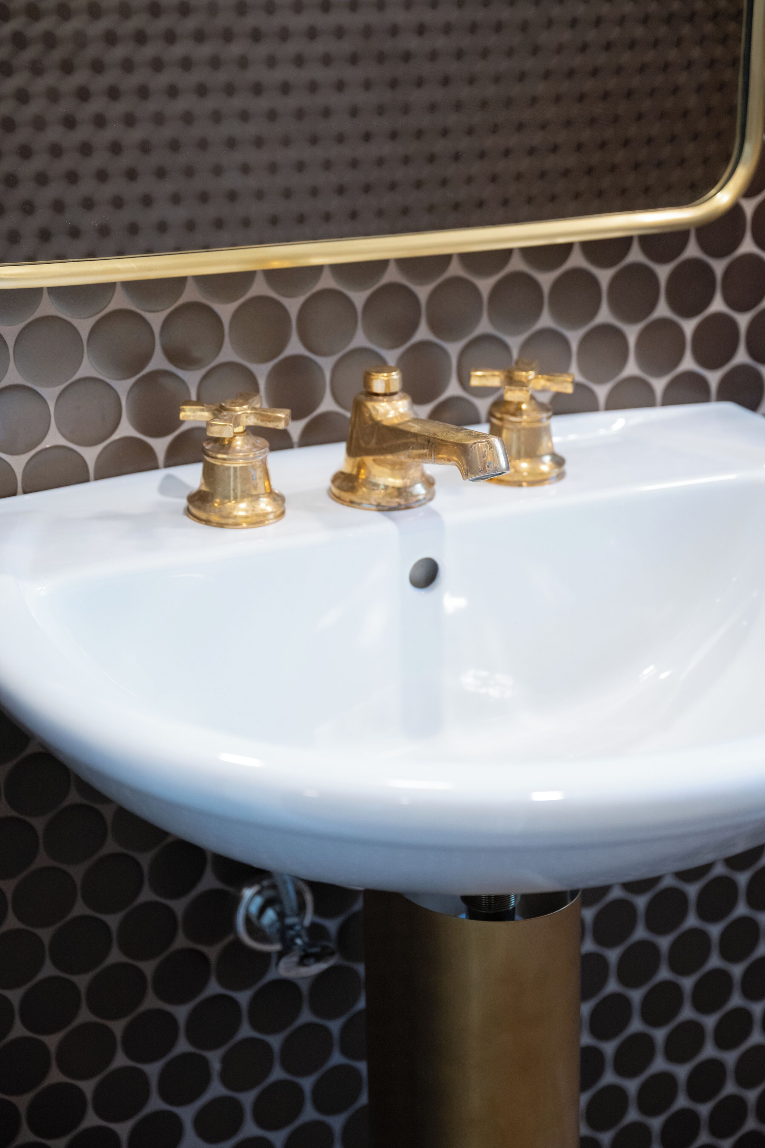 A white sink with gold faucets and a gold base, set against a patterned wall.