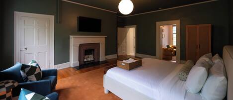 Een slaapkamer met een groot bed, een open haard, een bank en een kledingkast.
