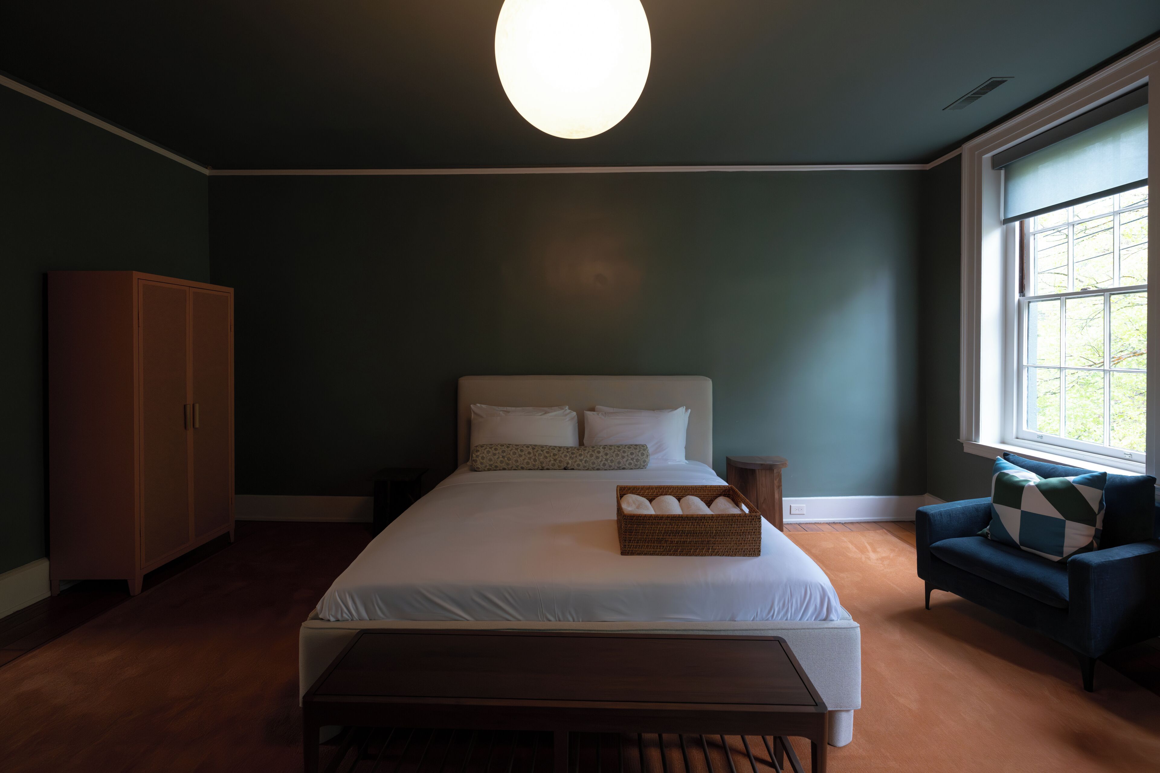 A bedroom with a large bed, a wooden bench, a dresser, and a window with a view.
