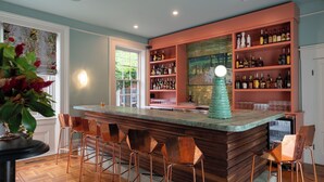 A bar area with wooden bar stools, a bar counter, and shelves with bottles. - The Ashbrook Hotel (Frankfort)