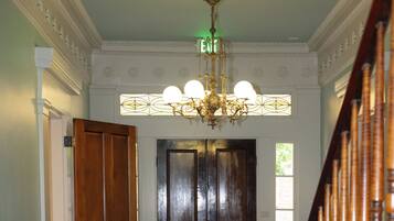 A grand hallway with a wooden staircase, a chandelier, and a green carpet.