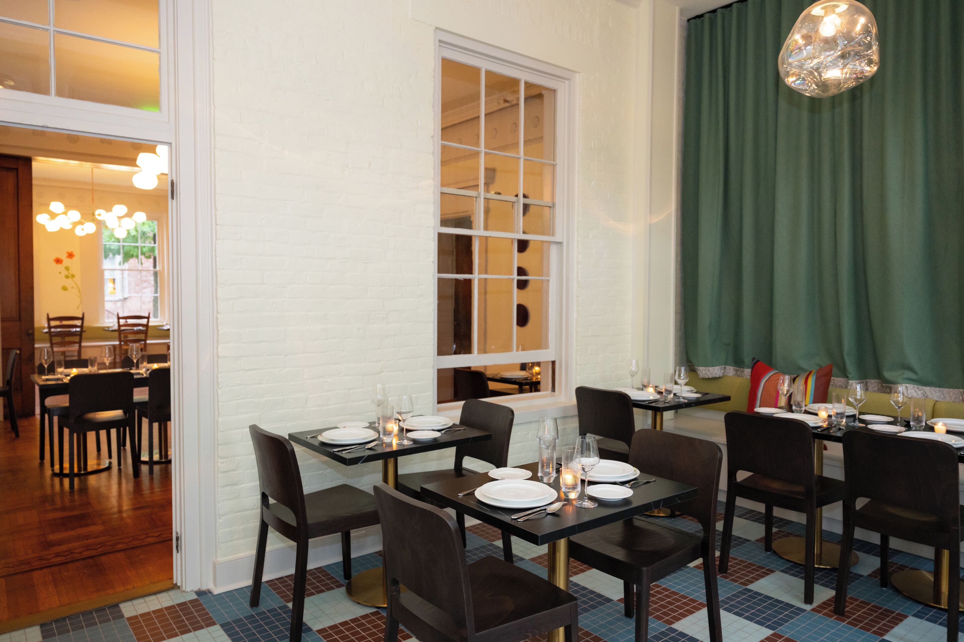 A restaurant with tables set for dining, a large window, and a green curtain.