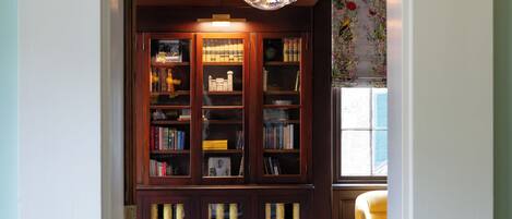 A cozy reading nook with a wooden bookshelf, a round table with a vase, and a comfortable armchair.