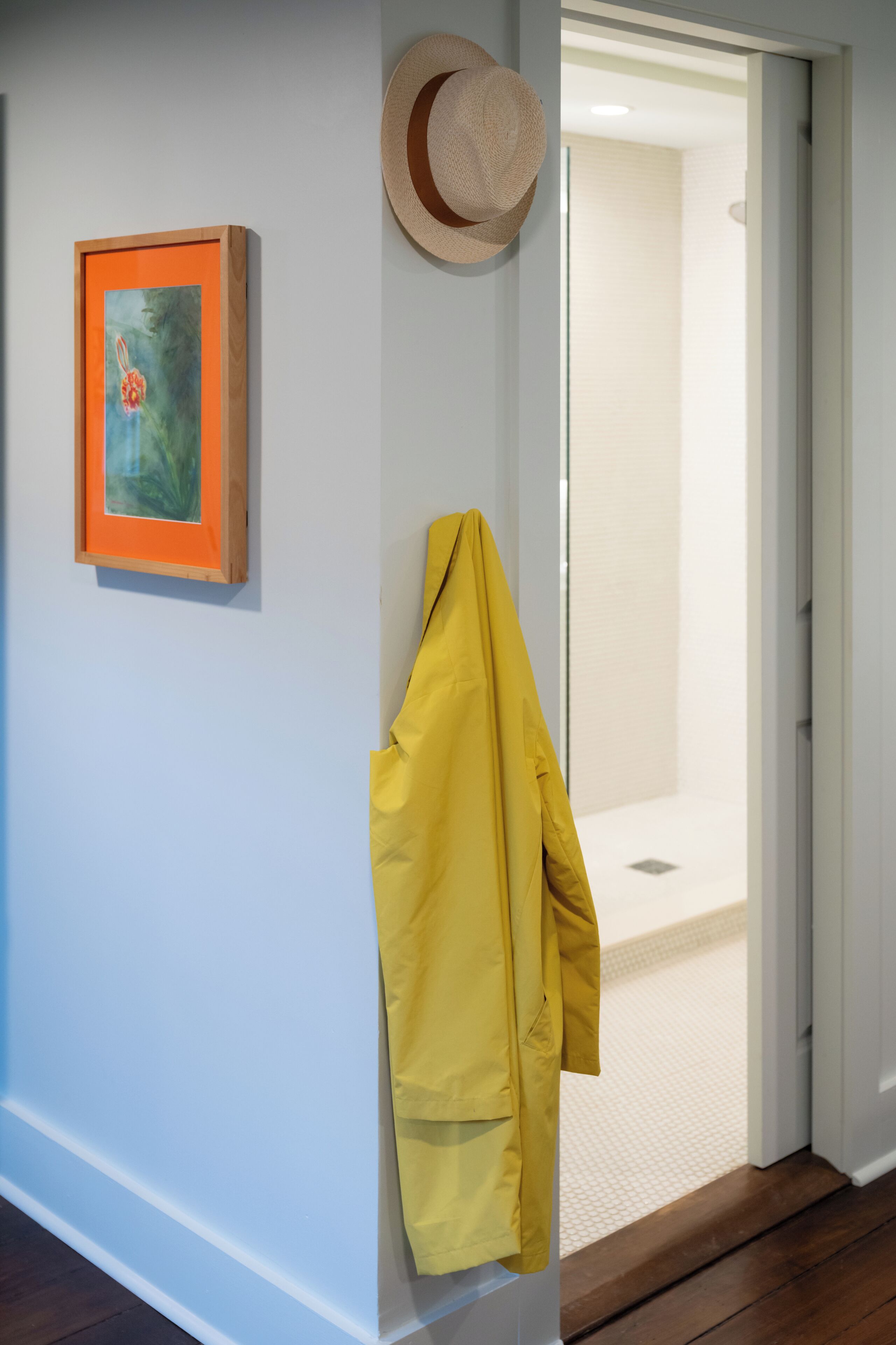 Un pasillo con un cuadro enmarcado, un sombrero de paja y una chaqueta amarilla colgados en la pared.