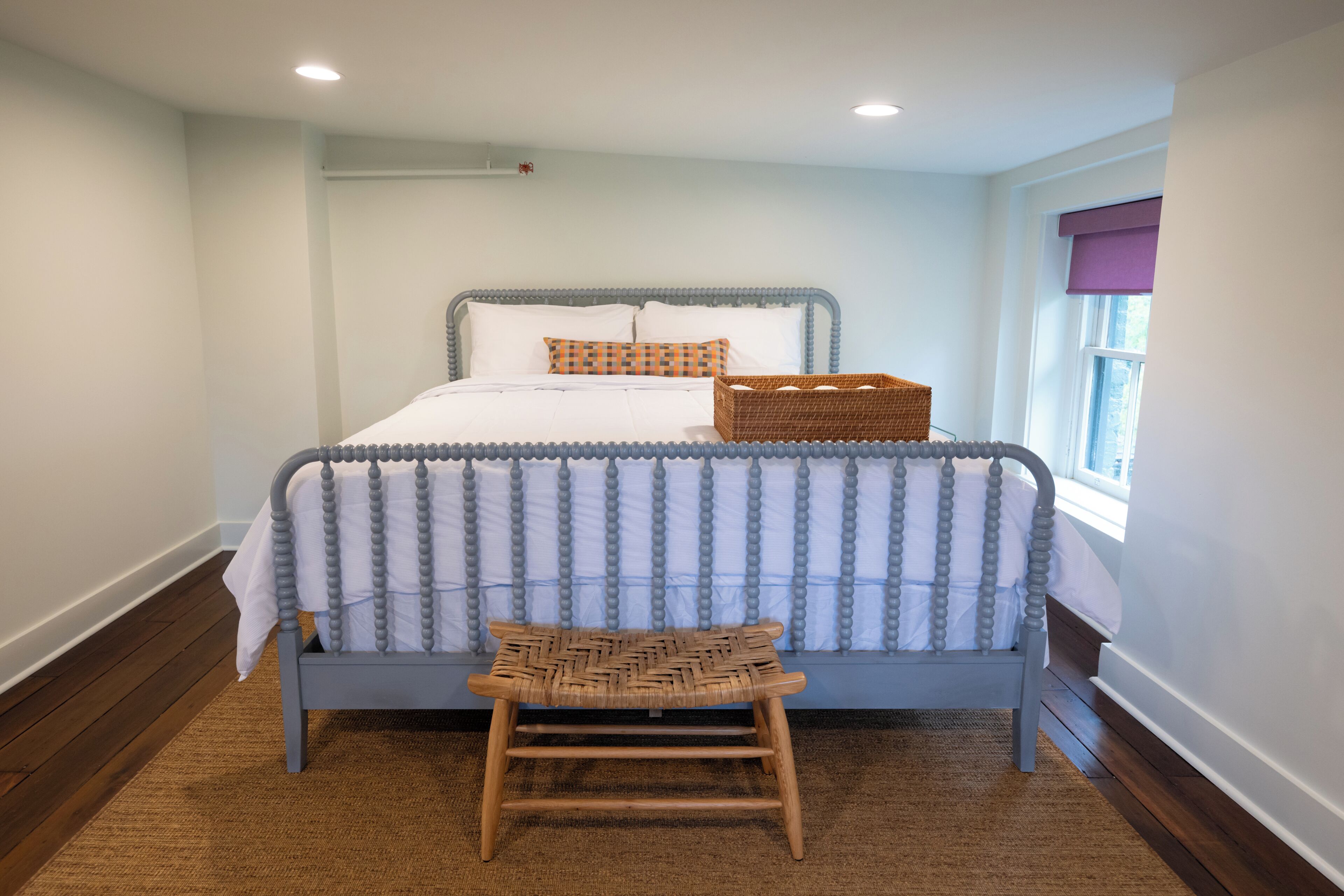 A bedroom with a bed, a small stool, and a window with a view.