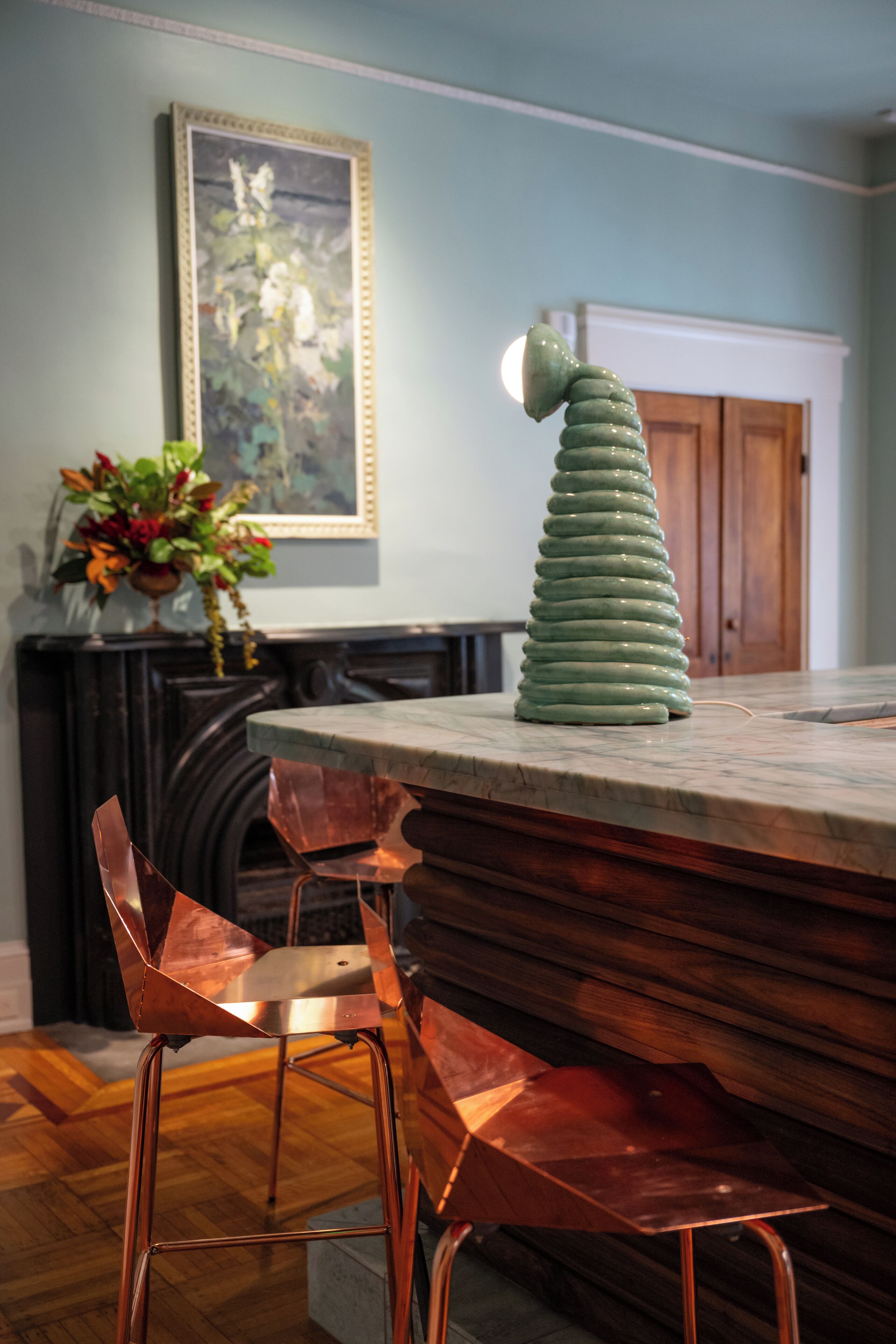 Una cocina con encimera de mármol, sillas de cobre y un objeto decorativo verde.