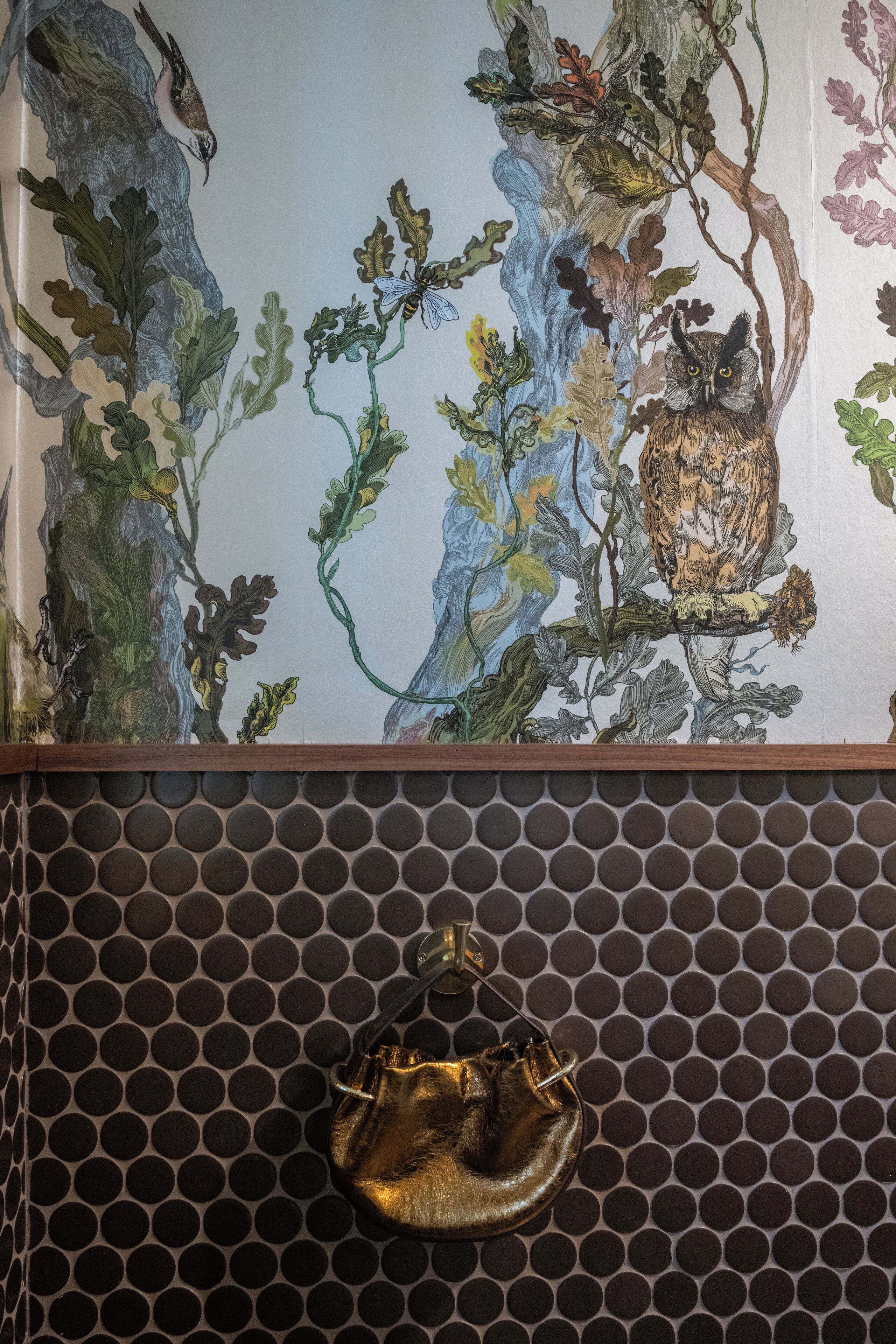 A wall with a mural of a tree and an owl, and a hanging gold-colored bag.