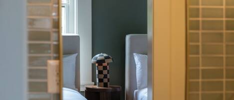 A bathroom with a white sink, gold faucets, and a mirror reflecting a bed with a checkered lamp.