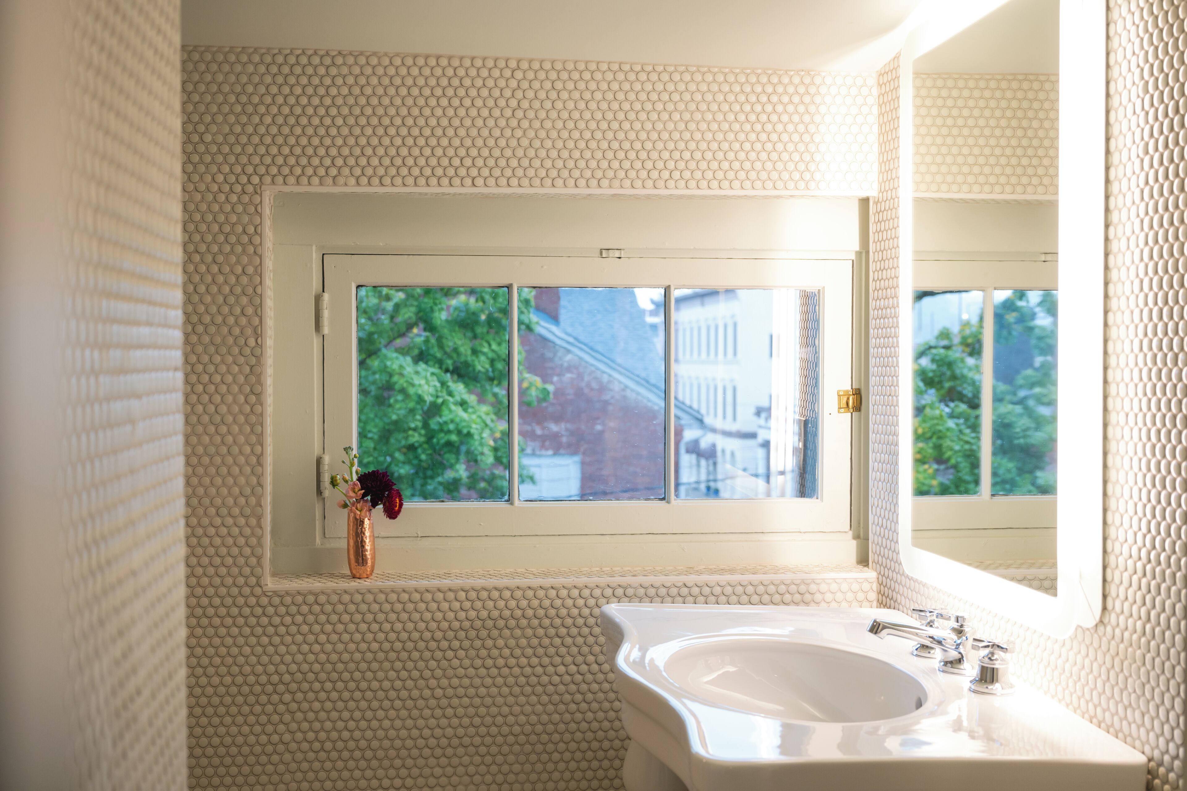 Une salle de bain avec une fenêtre, un lavabo et un vase rempli de fleurs.