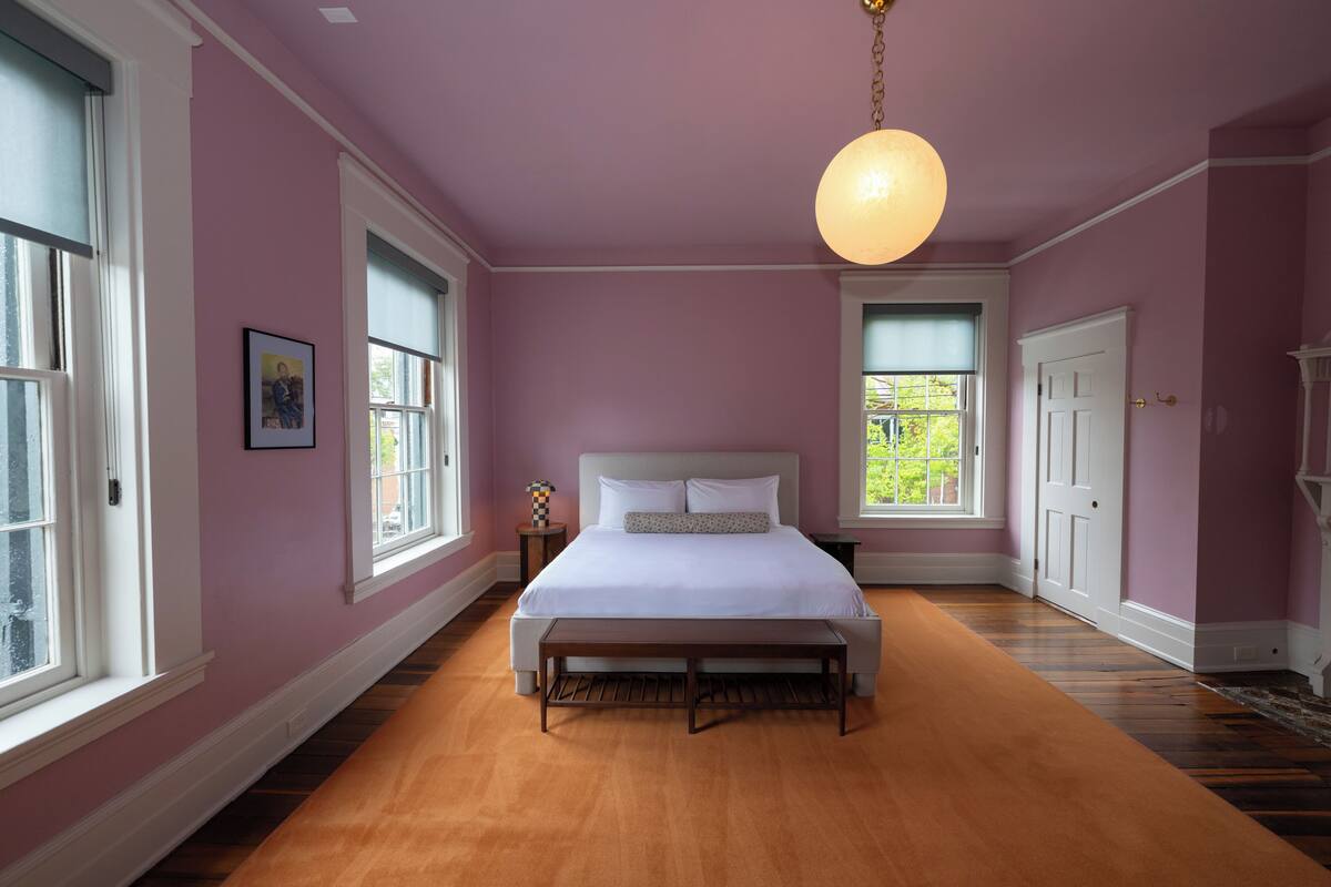 A bedroom with a large bed, a bench, and two windows.